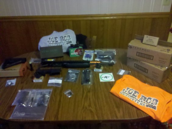 Various gun parts and accessories, including firearms and apparel, laid out on a wooden table