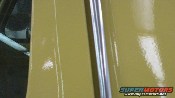 Yellow car door with chrome trim strip, showing reflections and minor paint imperfections