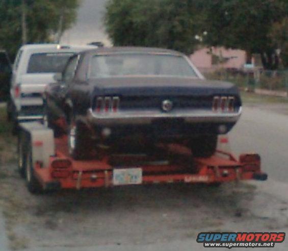1967 Ford Mustang on a red trailer, with a white vehicle partially visible behind it