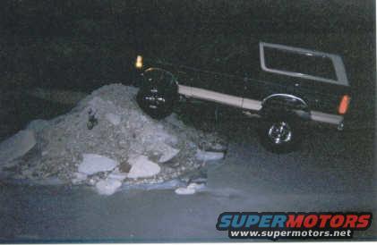 Black Ford Bronco driving over a pile of debris at night