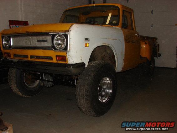1971 International pickup truck with yellow cab and orange bed, white fender. Lifted with large tires