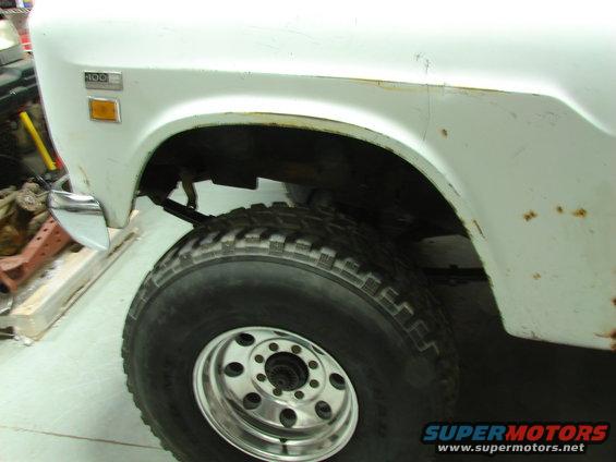 Close-up of a white International pickup truck's front fender and large tire. Badge reads '100'