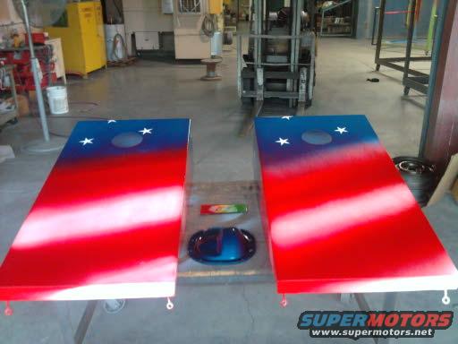 two cornhole boards painted red, white, and blue with stars, sitting in a workshop with a forklift in the background