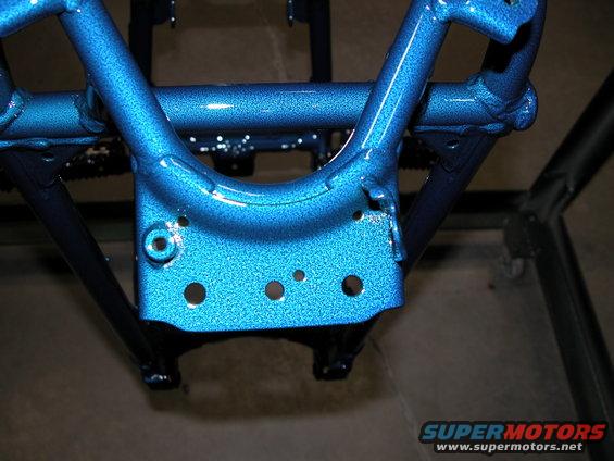 Close-up of a blue metallic painted vehicle frame section with several bolt holes