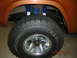 1973 Ford Bronco - Close-up of an orange SUV's wheel well, bright blue shocks and an off-road tire with visible tread detail.