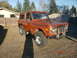 1973 Ford Bronco - This orange SUV is parked in a residential driveway with a house and fence in the background.