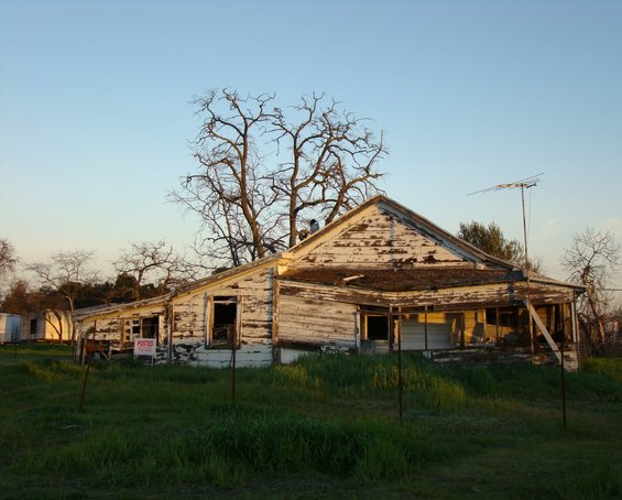 dilapidated house with peeling paint, broken windows, and overgrown grass. A 'posted' sign is visible
