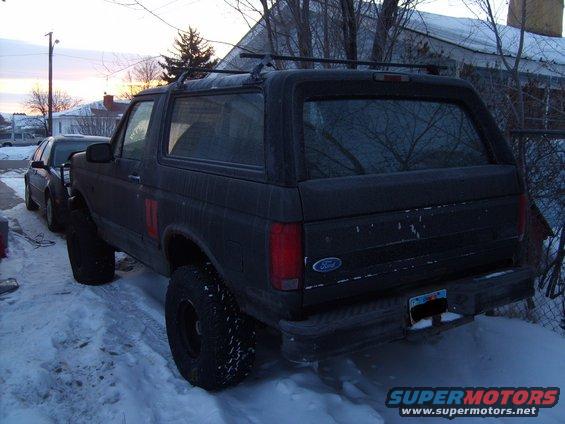 Dark gray Ford Bronco with roof rack parked in snow, rear 3/4 view