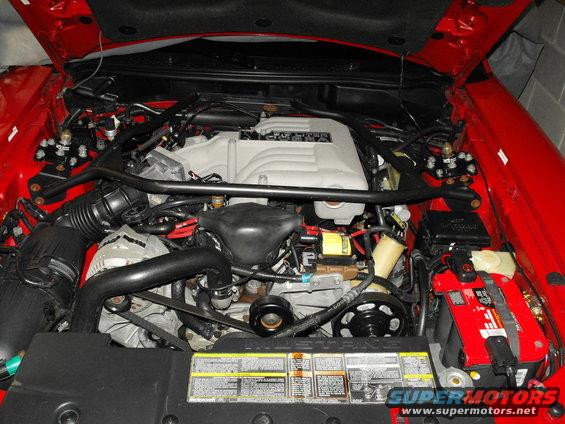 Red engine bay with V8 engine, air intake, and battery