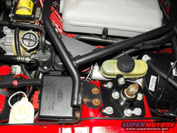 Engine bay with red fluid reservoir, black fuse box with Ford logo, and red spark plug wires