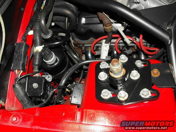 Engine bay with red painted metal, black hoses, wiring, and a black metal bracket with bolts