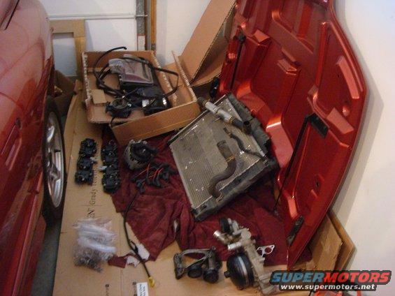 Red car hood and engine parts including a radiator and ignition coils on a garage floor