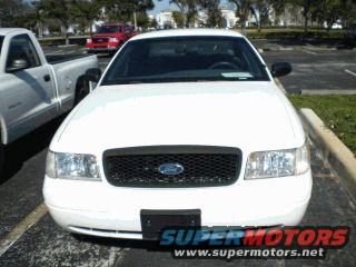 White 2002 Ford Crown Victoria parked in a lot, front view. Red Ford F-150 in background