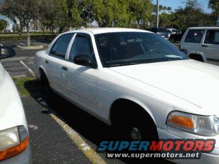 White sedan parked in a lot. Another vehicle is partially visible on the right