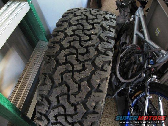 Off-road tire with aggressive tread pattern, next to a green ladder and bicycle components
