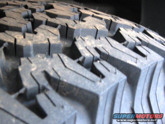 Close-up of a knobby off-road tire tread. Text at bottom says SUPERMOTORS.NET