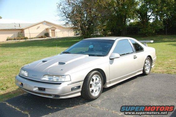 Silver 1991 Ford Thunderbird coupe with aftermarket hood scoops and a rear spoiler parked on a driveway