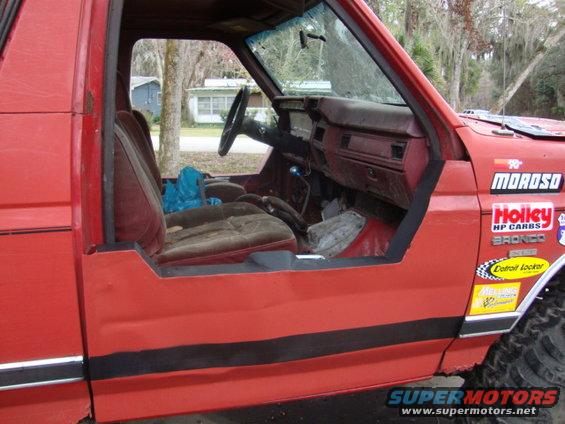 Red 1986 Ford Bronco interior with half doors and racing decals on the exterior