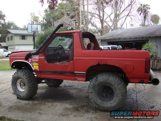 Red off-road SUV with snorkel, removed doors, and large tires. Visible 'Supermotors' watermark