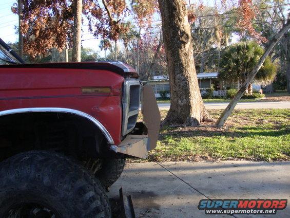 Front corner of a red truck with a custom bumper being fitted. Large tires are visible