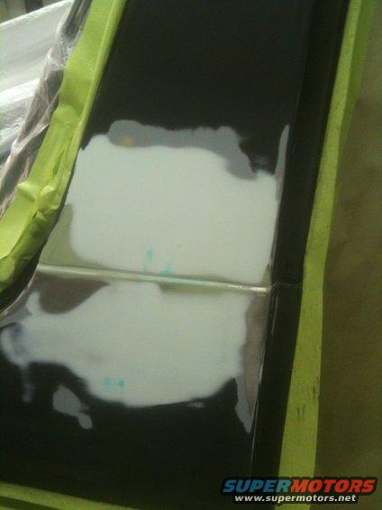 Black car tailgate with body filler and green masking tape
