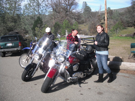 Green SUV parked next to two motorcycles with people around them