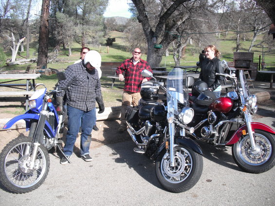 Three motorcycles parked with four people standing around them