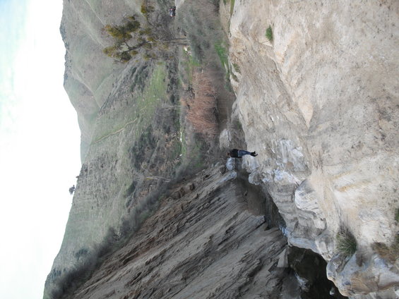 Person in dark clothing sits on the edge of a rocky cliff overlooking a valley