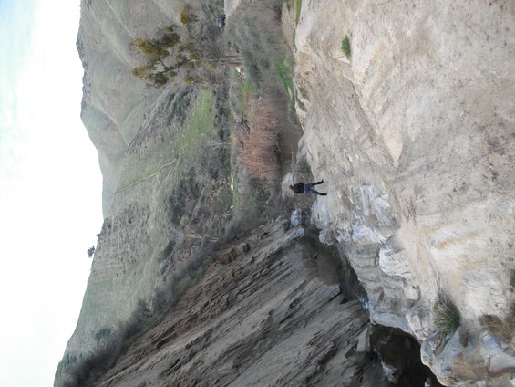 Person rappelling down a rocky cliff face with a grassy hillside in the background