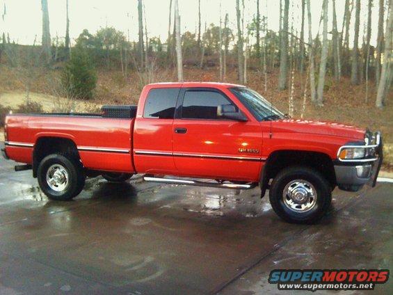 Red Dodge Ram pickup truck, side view. Has a toolbox in the bed and a brush guard on the front