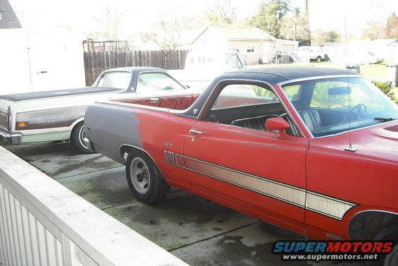 1970 Ford Ranchero in red with gray primer on the rear quarter panel, parked next to a white and woodgrain Ranchero