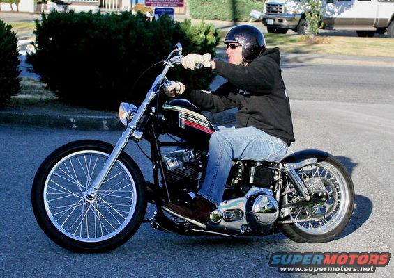 Man wearing a helmet and jeans rides a black custom motorcycle with spoked wheels