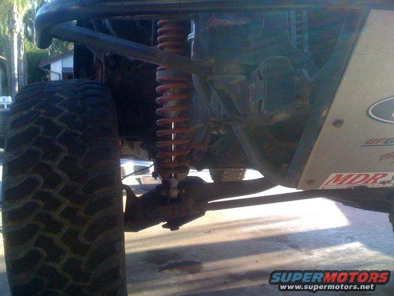 Off-road vehicle suspension with large tire, red coilover shock, and metal skid plate with MDR sticker