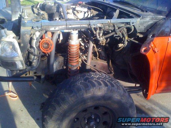 Off-road truck front view, exposed engine, orange suspension spring, large tire