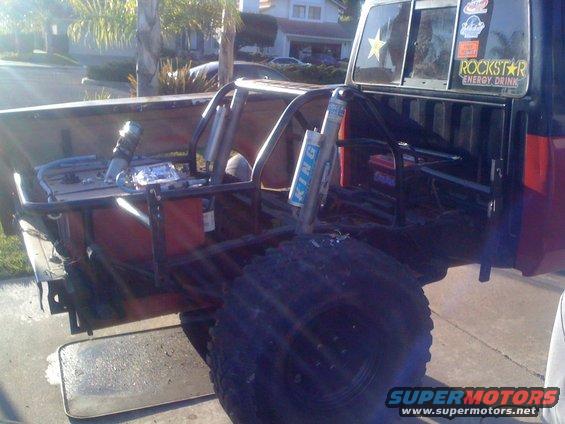 Custom roll cage installed in the bed of a pickup truck, with large off-road tires visible