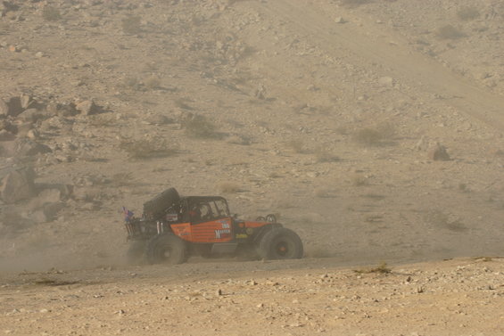 Orange off-road buggy with spare tire on back driving on dusty desert terrain