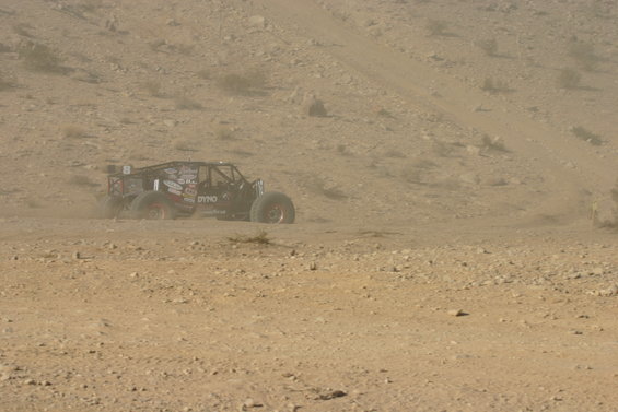 Off-road buggy with roll cage and large tires driving on a dusty desert terrain