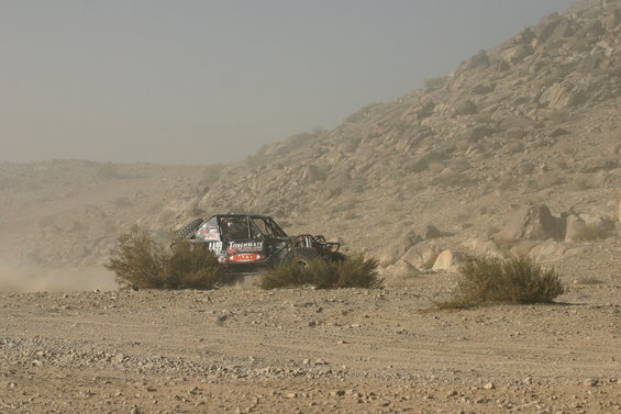 Black off-road buggy with red and white decals driving through a dusty desert landscape