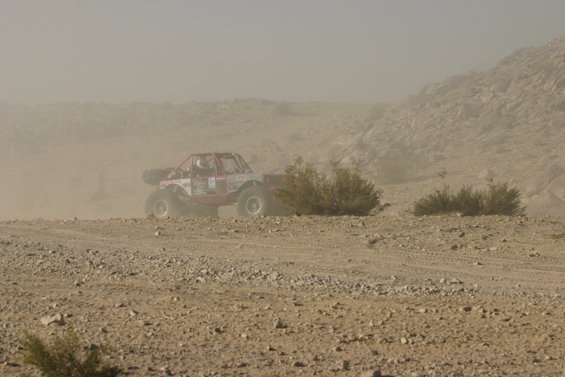 Red off-road buggy kicking up dust on a rocky desert terrain