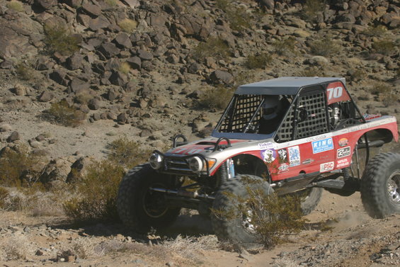 Red and silver off-road buggy with large tires and a roll cage, number 70 on the roof, driving on a rocky desert terrain