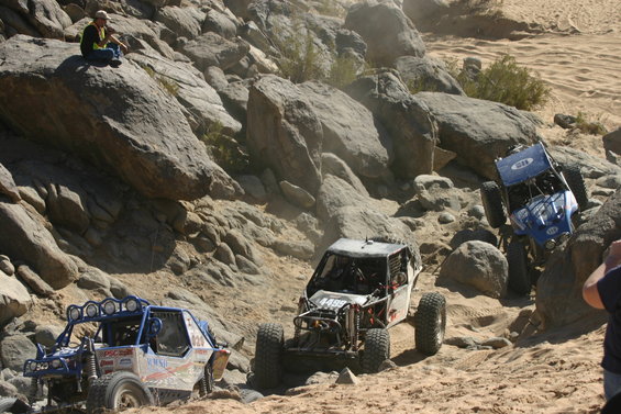 Three off-road vehicles navigating a rocky desert terrain