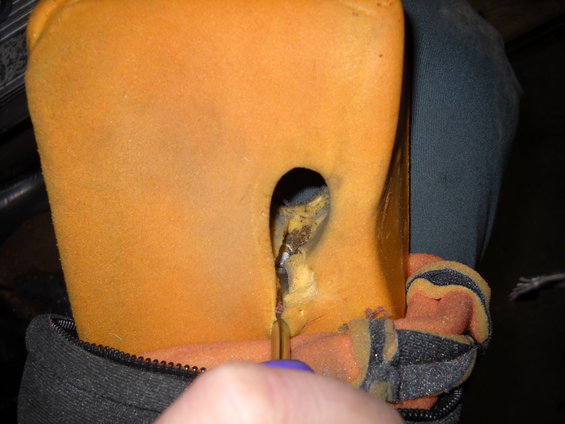 Close-up of torn orange car seat foam with exposed stuffing and a tool poking through