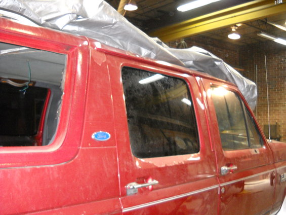 Red Ford van side view, covered with a tarp. Visible Ford badge
