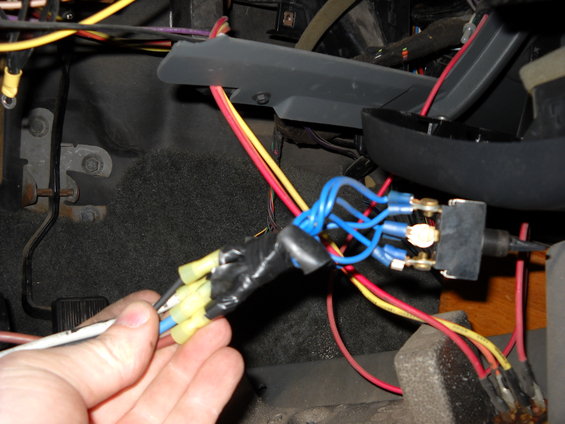 Hand holding blue and yellow wires connected to a switch, with black electrical tape and red and yellow wires visible