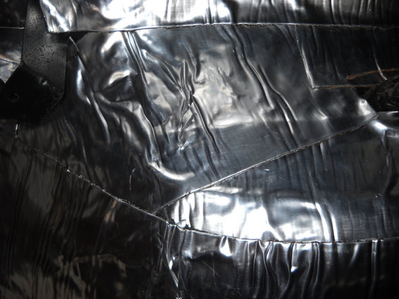 Close-up of shiny, wrinkled black interior upholstery with visible stitching
