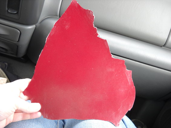 Hand holding a torn piece of red trim inside a vehicle. Interior dash visible