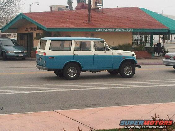 Two-tone blue and white SUV driving past a Los Tacos restaurant
