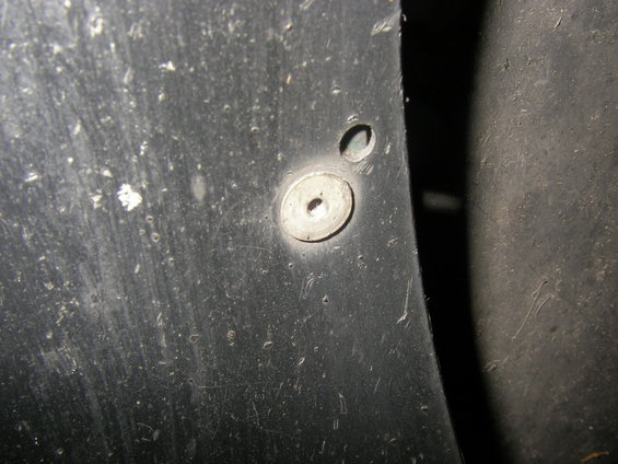 Black plastic fender flare with a silver screw and washer, showing scuffs and dirt
