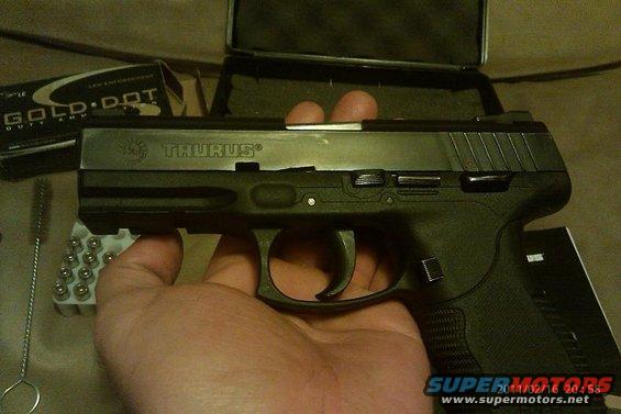 Hand holding a Taurus pistol, box of Gold Dot ammo, and cleaning brush