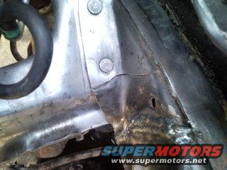Close-up of damaged metal on a vehicle frame, showing welds and a hole